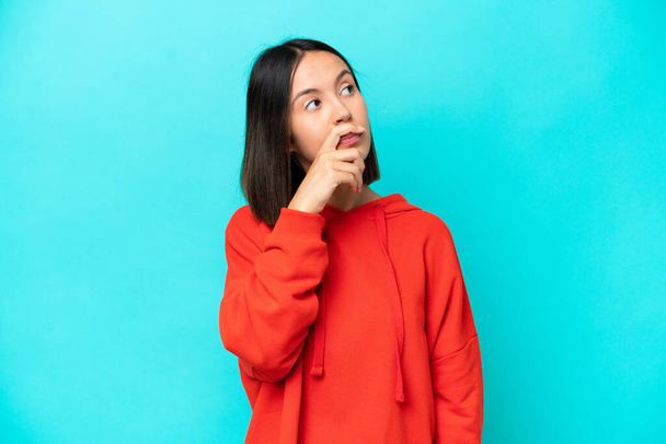 Young caucasian woman isolated on blue background making doubts gesture - Photo, Image