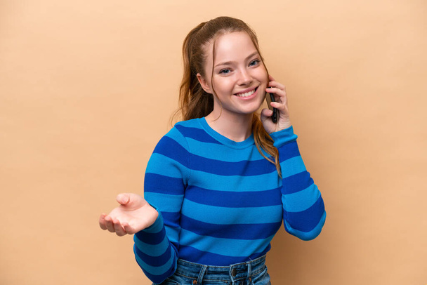 Joven mujer caucásica aislada sobre fondo beige manteniendo una conversación con el teléfono móvil con alguien - Foto, imagen