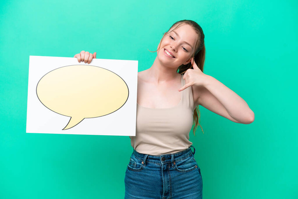 Young caucasian woman isolated on green background holding a placard with speech bubble icon and doing phone gesture - Photo, Image