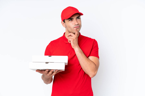 Pizza consegna uomo caucasico con uniforme di lavoro raccogliendo scatole di pizza isolate su sfondo bianco avendo dubbi mentre guardando in alto - Foto, immagini