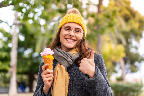 Bruna donna con un gelato alla cornetta all'aperto con i pollici in su perché è successo qualcosa di buono - Foto, immagini