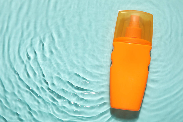 Fles zonnebrandcrème in water op kleur achtergrond - Foto, afbeelding