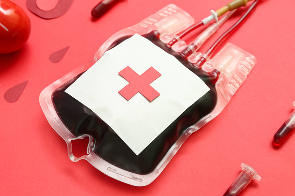 Envase de sangre con tubos y gotas de papel sobre fondo rojo, primer plano. Día Mundial del Donante - Foto, Imagen