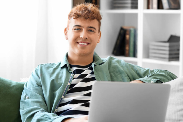 Young redhead man using laptop on sofa at home, closeup - Foto, immagini
