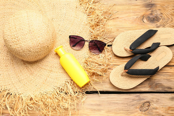 Sluneční brýle s žabkami, proutěný klobouk a láhev krému na opalování na dřevěném pozadí - Fotografie, Obrázek