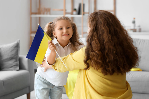 Gelukkig klein meisje en haar moeder met Oekraïense vlaggen in de woonkamer - Foto, afbeelding
