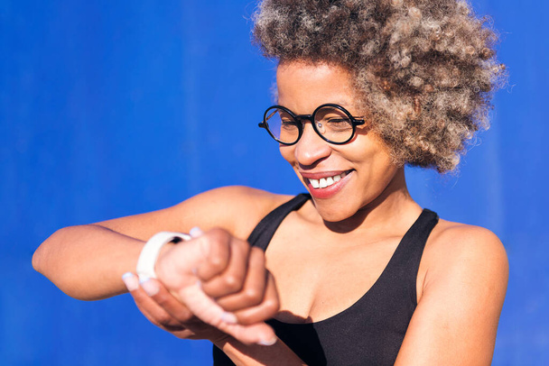 sporty african american woman using smart watch outdoors in a sunny day, concept of sports technology and active lifestyle, copy space for text - Φωτογραφία, εικόνα