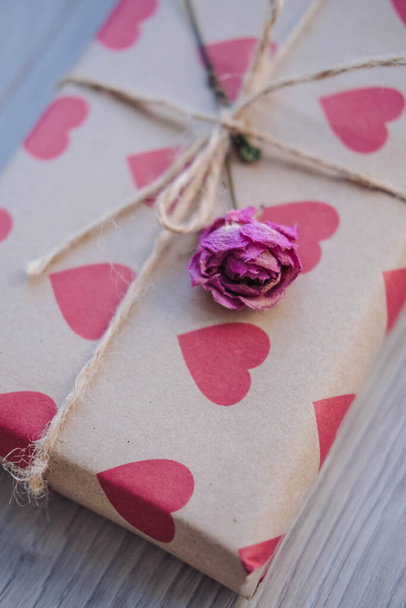 Caja de regalo envuelta en papel artesanal con corazones rojos sobre un fondo de madera - Foto, imagen