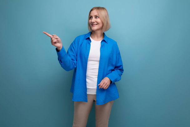 50 років жінка в синій сорочці з ідеєю на синьому фоні з копіювальним простором. - Фото, зображення