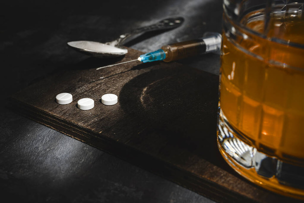Witte verdovende pillen, alcohol in een glas, injectiespuit met een dosis drugs op donkere achtergrond. Begrip verslaving, misbruik en slechte gewoonten. - Foto, afbeelding