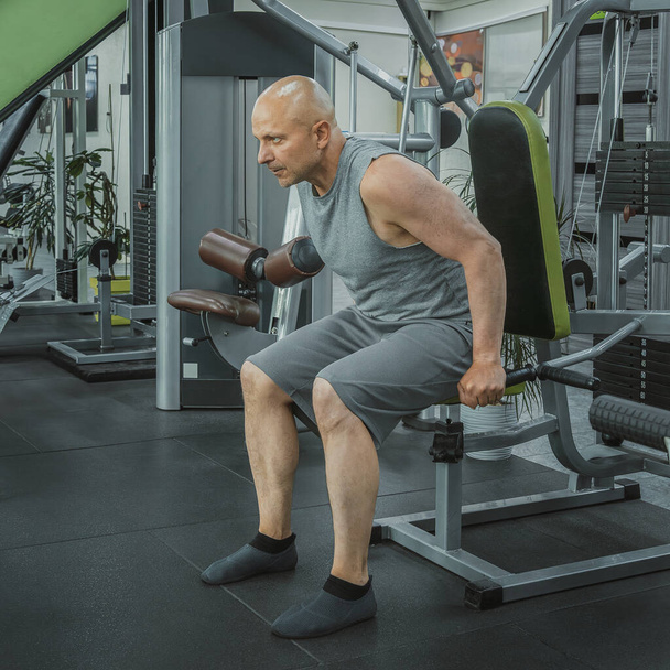 Чоловік сидить в симуляторі і виконує вправи для накачування трицепсів в спортзалі - Фото, зображення