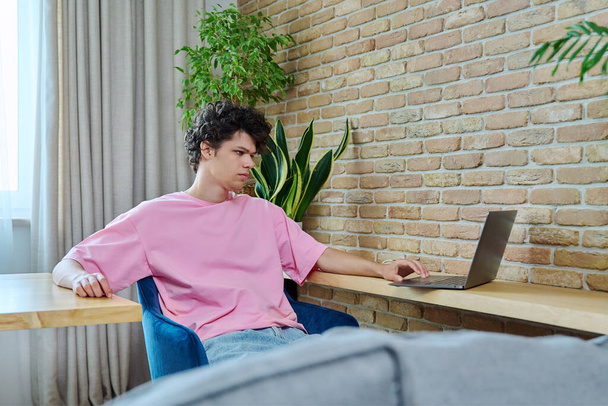 Handsome guy 19-20 years old student typing on laptop, sitting at desk at home. Use internet online technologies for study, work, life, leisure, communication - Zdjęcie, obraz