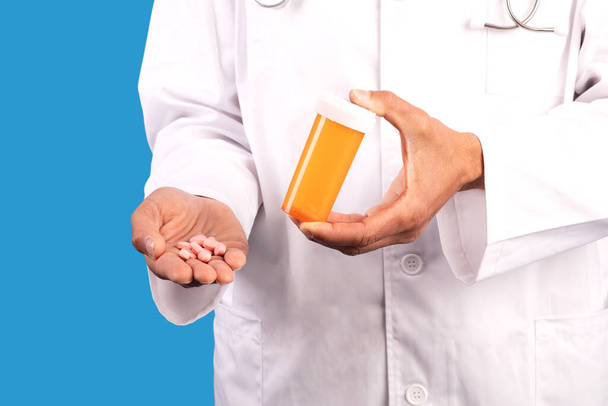 Schnappschuss eines professionellen Arztes, der Tabletten und Flasche in den Händen zeigt und auf blauem Hintergrund eine medikamentöse Behandlung des Patienten empfiehlt. Unbekannter Arzt zeigt Medikament - Foto, Bild