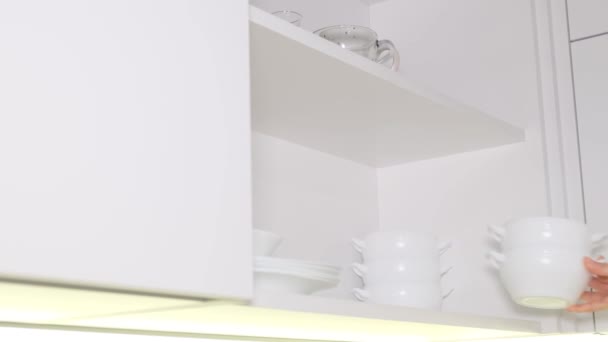 Una donna mette dei piatti bianchi puliti sul comodino in cucina. Lavarsi i piatti. Cucine moderne, organizzazione.  - Filmati, video