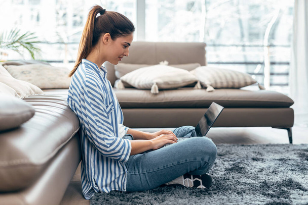 Shot of pretty young woman using her laptop while sitting on the floor at home - Photo, Image