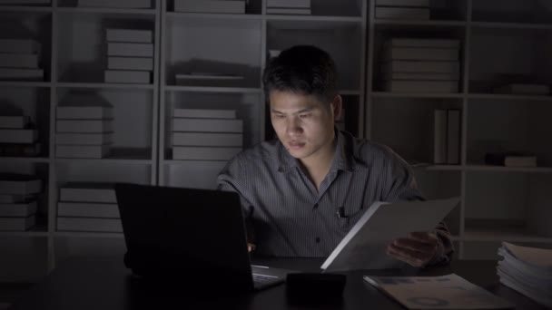 Asyalı erkek işadamı mali belgelerle ve masaüstü bilgisayarlarıyla geç saatlere kadar çalışıyor. Maaşlı çalışan genç adam konsepti 4K - Video, Çekim