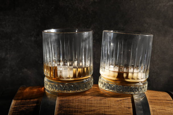 Glasses of cold whiskey on wooden barrel against dark background - Фото, изображение