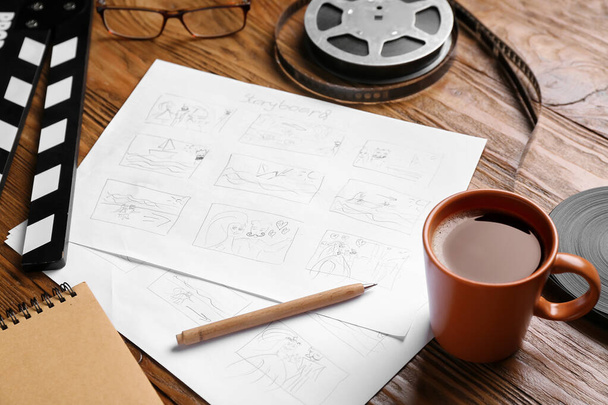 Storyboard with movie clapper, film reel and cup of coffee on wooden background - Photo, Image