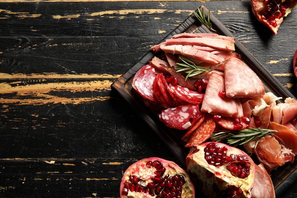 Board with assortment of tasty deli meats on dark wooden background - Фото, изображение