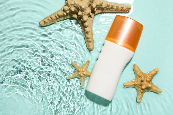 Crème solaire avec étoiles de mer dans l'eau sur fond de couleur - Photo, image