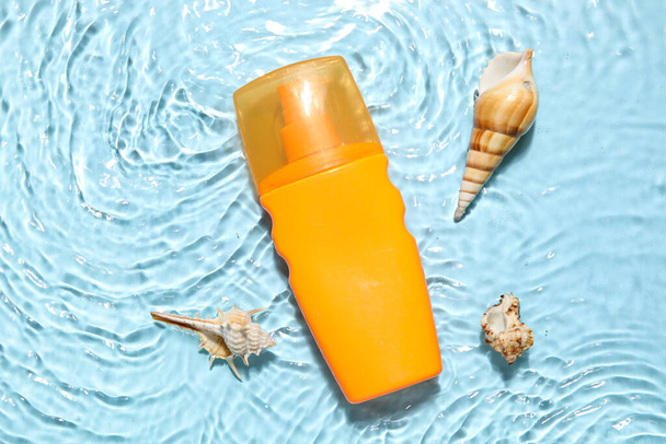 Sunscreen cream with starfishes and seashells in water on color background - Foto, imagen