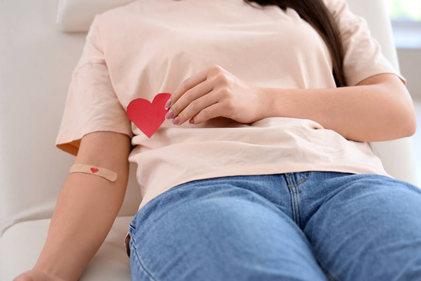 Donneur de sang féminin avec patch médical appliqué et coeur en papier en clinique, gros plan - Photo, image