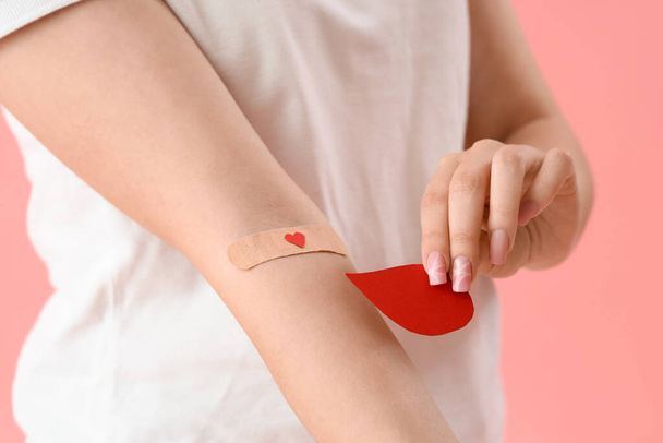 Donneur femelle avec patch médical appliqué et goutte de sang en papier sur fond rose, gros plan - Photo, image