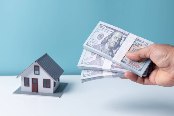 Vrouw met dollarbiljet in de hand met witte huis model achtergrond. Goedkeuring van hypothecair krediet - concept woninglening en verzekering. - Foto, afbeelding