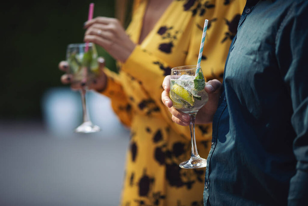 Ruce ženy a muže povzbuzují sklenicemi koktejlů. Pár oslav svatby, výročí s koktejly, s citronem a zeleninou Osvěžující alkoholický nápoj. Letní nápoje, svatba, párty. - Fotografie, Obrázek