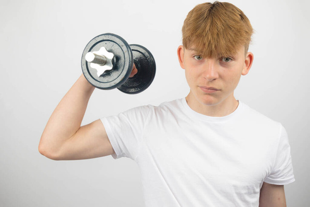 Portrait of a 14 year old caucasian teenage boy exercising with a dumbbell - Фото, изображение