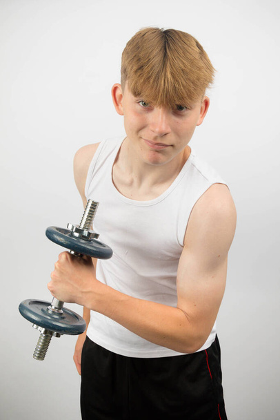 Portrait of a 14 year old caucasian teenage boy wearing a sleeveless vest using a dumbbell - Foto, afbeelding