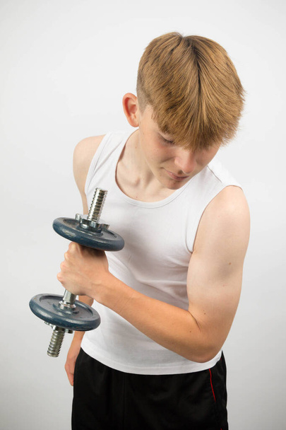 Portrait of a 14 year old caucasian teenage boy wearing a sleeveless vest using a dumbbell - Foto, Bild