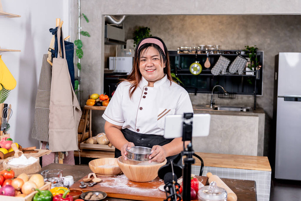 Eine asiatische dicke Frau steht in der Küche und bereitet Geräte vor, um Inhalt über Pizza hausgemacht zu machen. zu Influencer Marketing und Social Media Konzept. - Foto, Bild