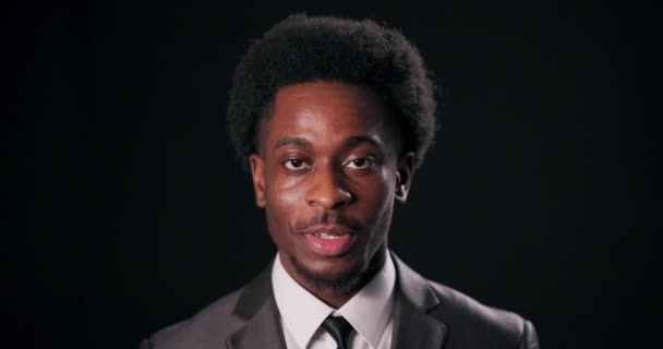 Magabiztos és összeszedett, egy afro-amerikai férfi okos öltönyben pózol és felvillan egy oké jelet, pozitivitást és bizonyosságot sugároz egy feltűnő fejlövéssel fekete háttér előtt.. - Felvétel, videó