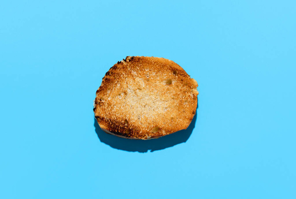 Vista superior con una rebanada tostada de pan de baguette, minimalista sobre una mesa azul. Rebanada de pan tostado aislada sobre un fondo azul. - Foto, imagen