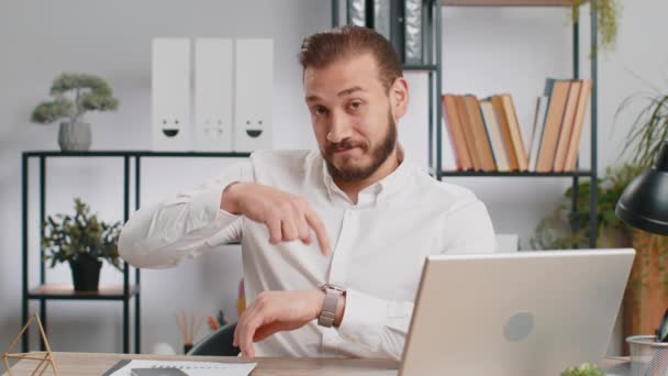 It is your time. Young middle eastern boss business man showing time on wrist watch clock, approve, pointing finger, time to start work, deadline. Freelancer guy at office workplace looking at camera - Footage, Video
