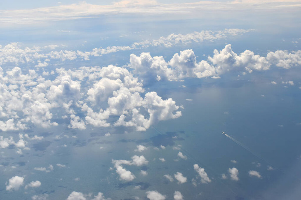 Betrachtet aus der Höhe des Flugzeugfensters durch weiße Wolken, die über dem Meer schweben. - Foto, Bild