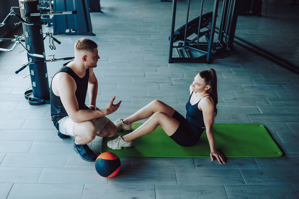 a personal trainer is seen having an informative conversation with a female client at the gym, providing valuable assistance and explaining the intricacies of different exercises. - Photo, image