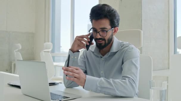 exitoso árabe hombre de negocios hablando teléfono en oficina hombre ejecutivo profesional empleador indio hombre amigable charla de negocios llamada móvil conversación en el lugar de trabajo teléfono celular sonriendo - Metraje, vídeo