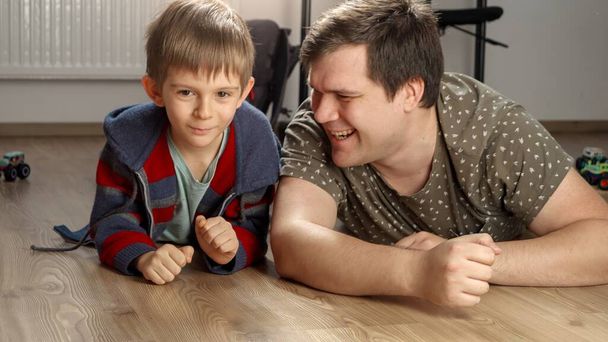 Щасливий усміхнений батько з сином лежить на підлозі в спальні і грає в ігри. - Фото, зображення