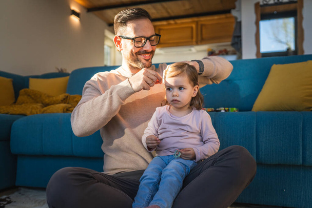Батько і дочка грають на підлозі вдома зрілий дорослий кавказький чоловік грає зі своєю дворічною дитиною малюк робить її батьківство волосся і пов'язує сімейний час концепції копіювання простору - Фото, зображення