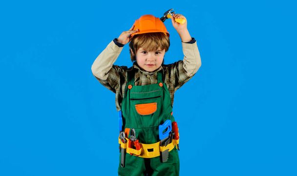 Маленький дитячий ремонтник у формі будівника з поясом для інструментів та молотком. Маленький хлопчик у хардхаті та комбінезоні з молотком. Хлопчик-будівельник у безпечному шоломі з іграшковими інструментами для ремонту або будівництва. Дитяча гра - Фото, зображення