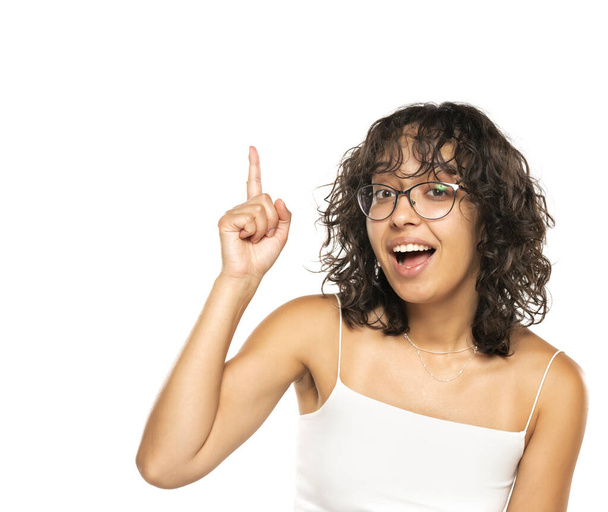メガネと波の髪を持つ若いダークスキーの幸せな女性は,白いスタジオの背景にアイデアを持っています - 写真・画像
