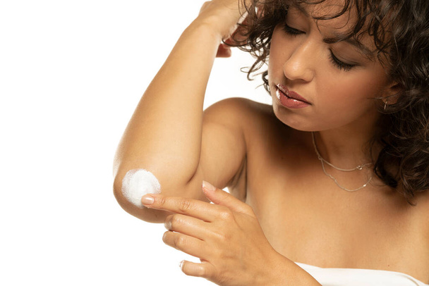 Head shot of a exotic woman takes care of her elbows using cosmetic cream on a white studio background - Photo, Image
