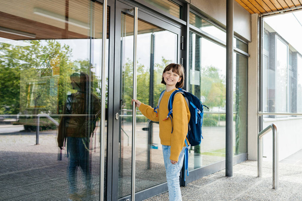 A teenage girl stands in front of the door to the school and opens it. Beginning of lessons and academic year. - Photo, Image