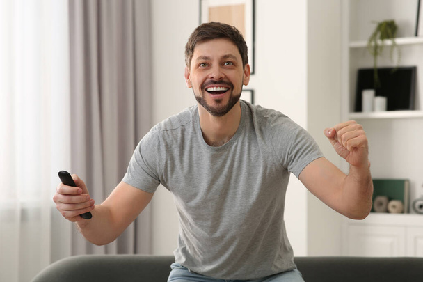 Emotional man holding remote controller and watching TV at home - Φωτογραφία, εικόνα