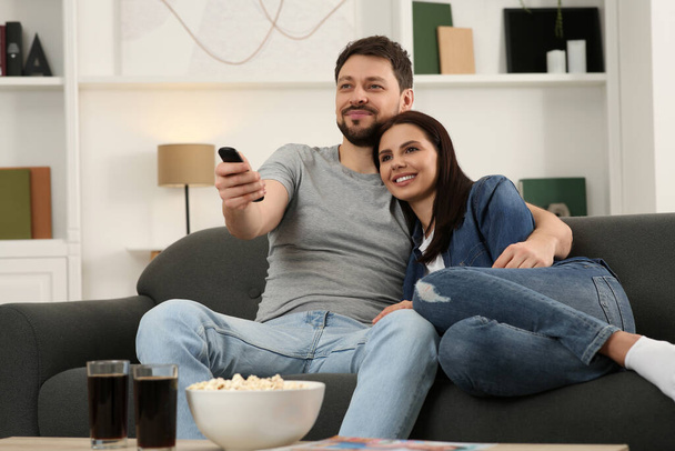 Happy couple watching show at home. Man changing TV channels with remote control - Foto, Imagem