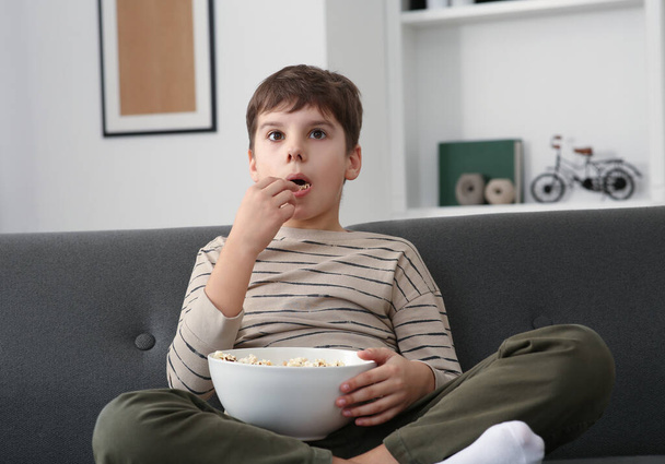 Маленький мальчик ест попкорн, когда смотрит телевизор дома - Фото, изображение