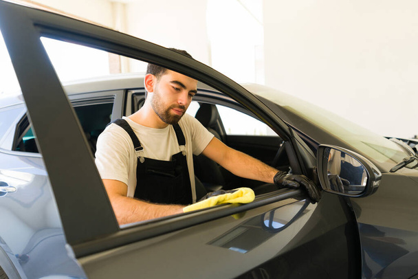 Bonito homem latino limpando as portas interiores do veículo de um cliente com um pano de lavagem na lavagem do carro - Foto, Imagem
