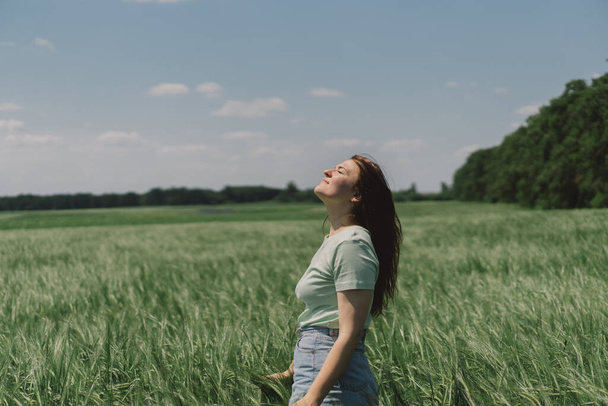 Uma mulher desfruta do ar fresco na natureza em um campo de cevada verde. Campo de verão e recolhendo flores. Momento de tranquilidade atmosférica - Foto, Imagem